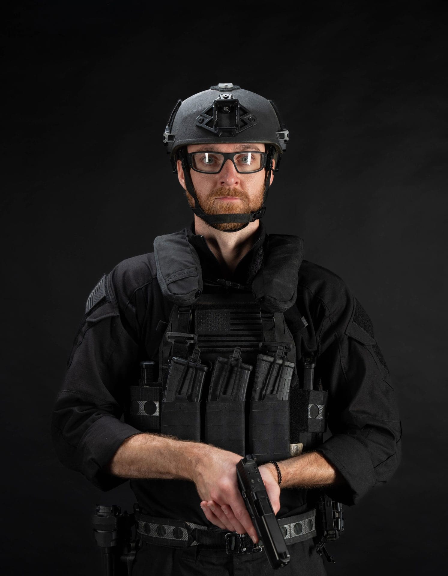 Personne en tenue tactique tenant une arme à feu sur fond noir.