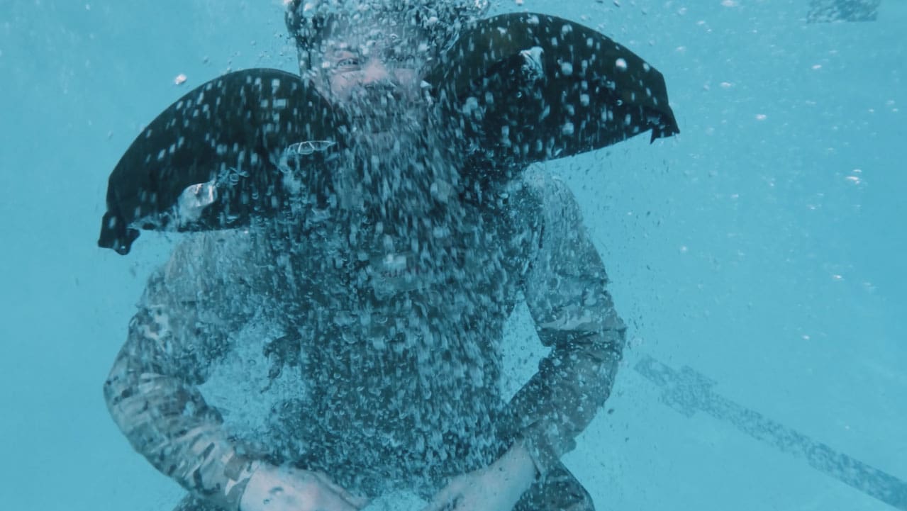 Personne immergée dans l'eau, des bulles entourant le corps, portant un vêtement sombre et le Galéo gonflé autour du cou.