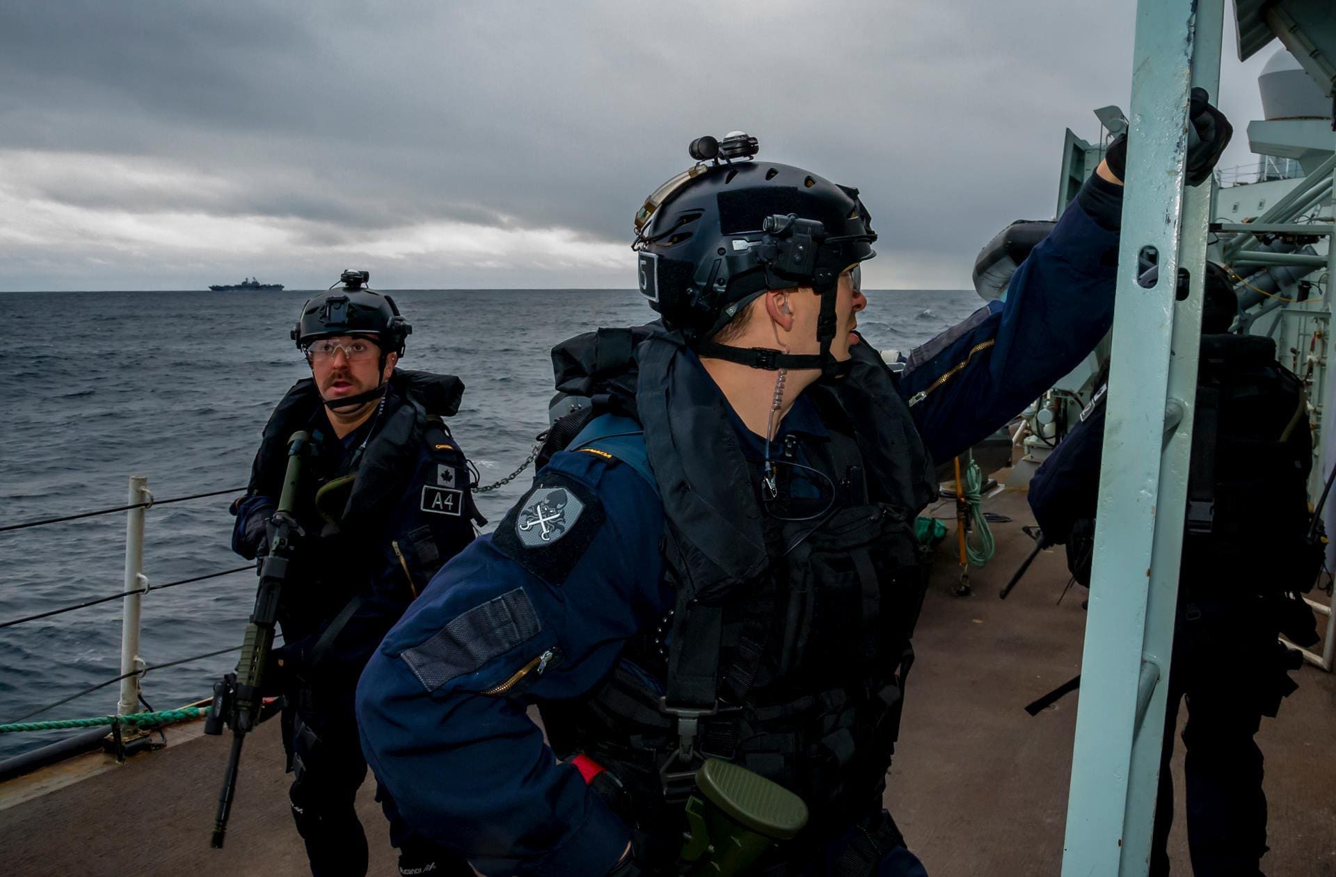 Personnel de la marine en tenue sur le pont d'un navire avec un navire au loin sur une mer couverte.