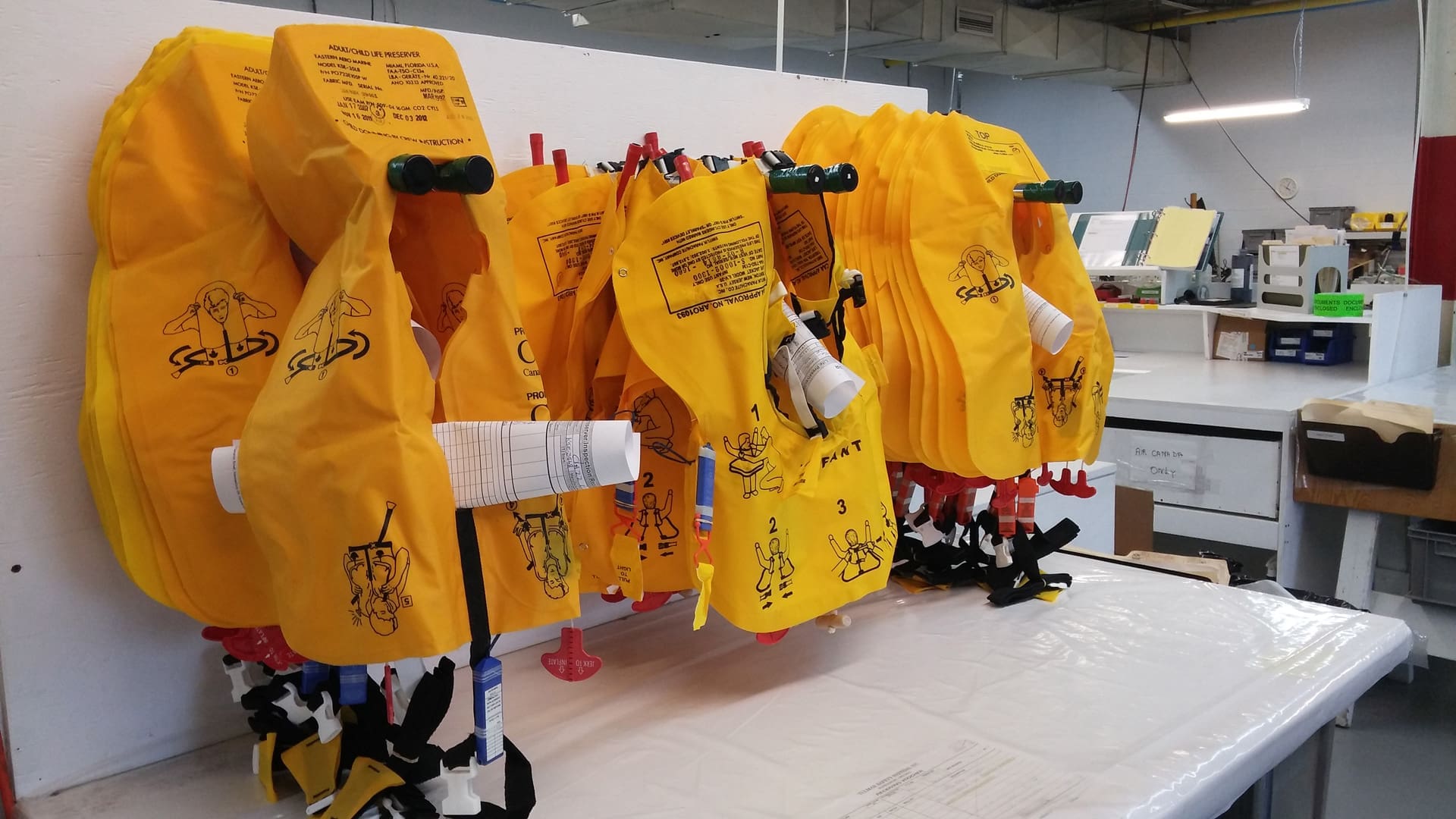 Yellow life jackets hang in a workshop, featuring illustrations and text for use instructions